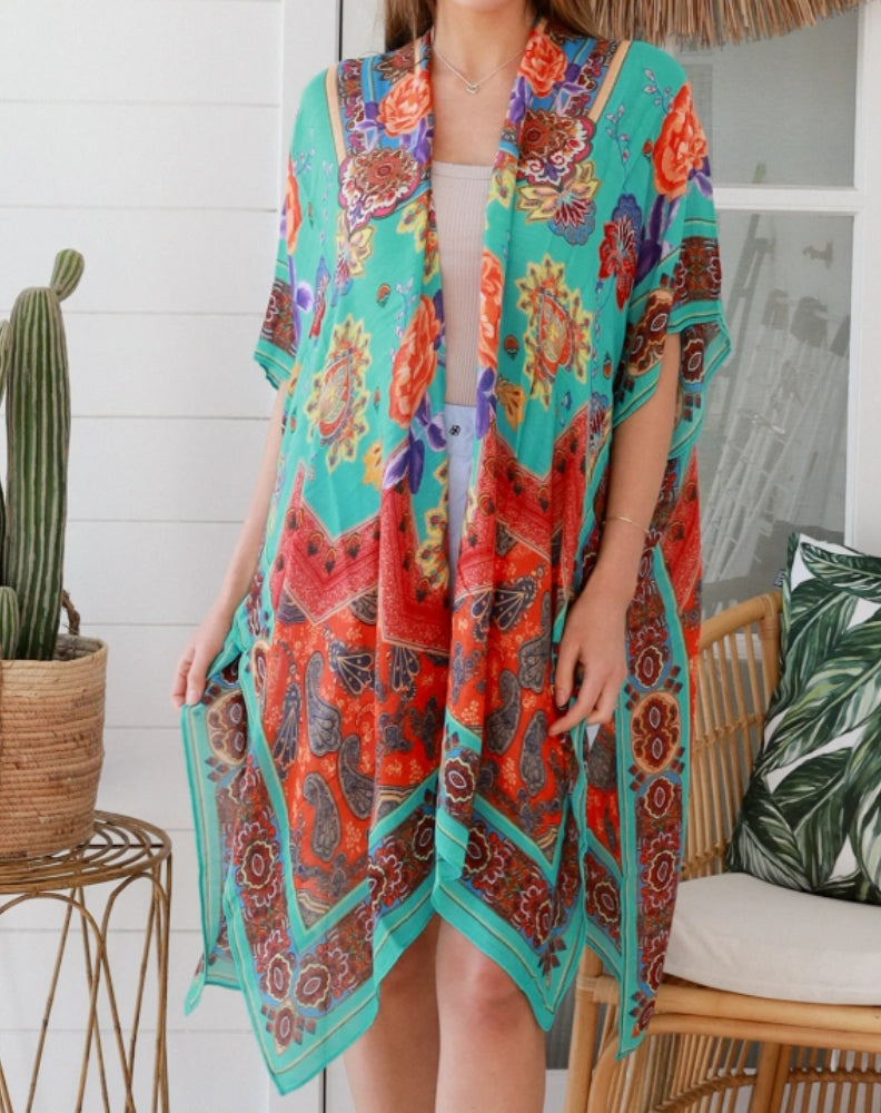 lady wearing floral aqua kimono in a home setting with a cactus and boho cane chair.