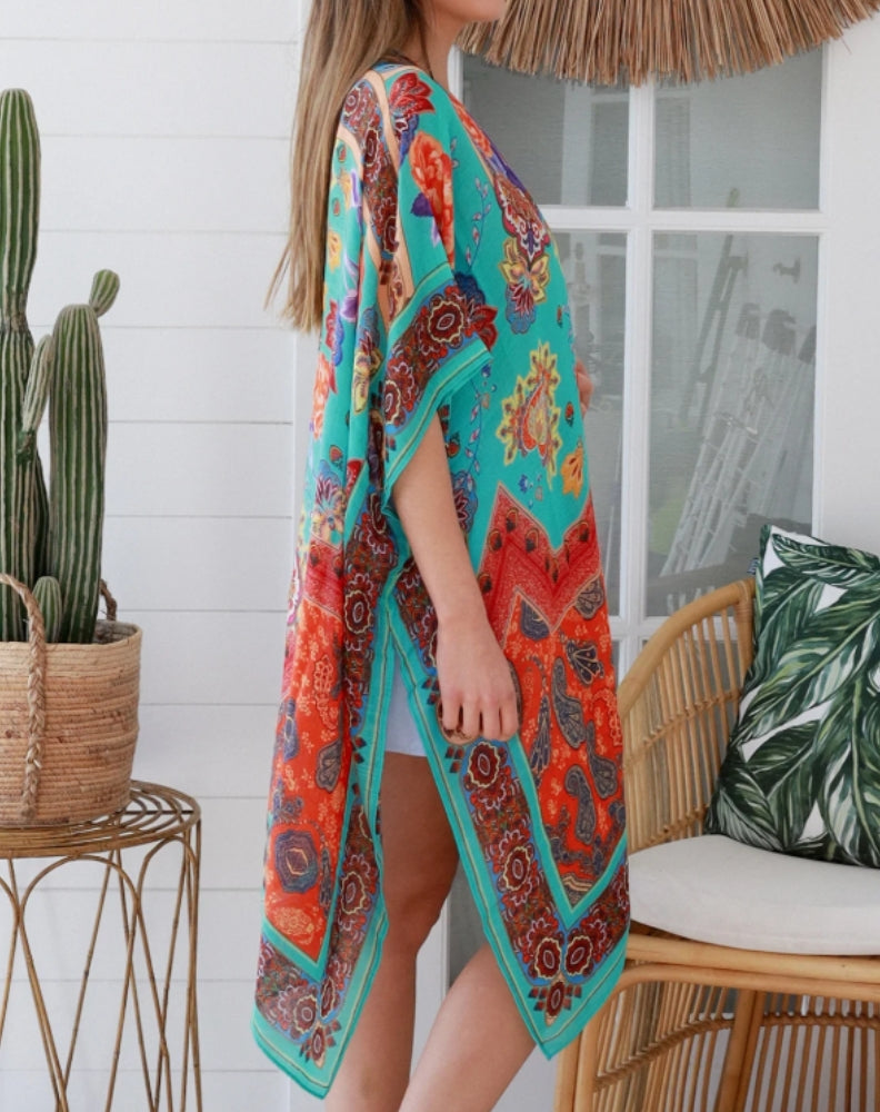 Woman wearing a aqua camilla beach cover-up in a home setting with a wicker chair.