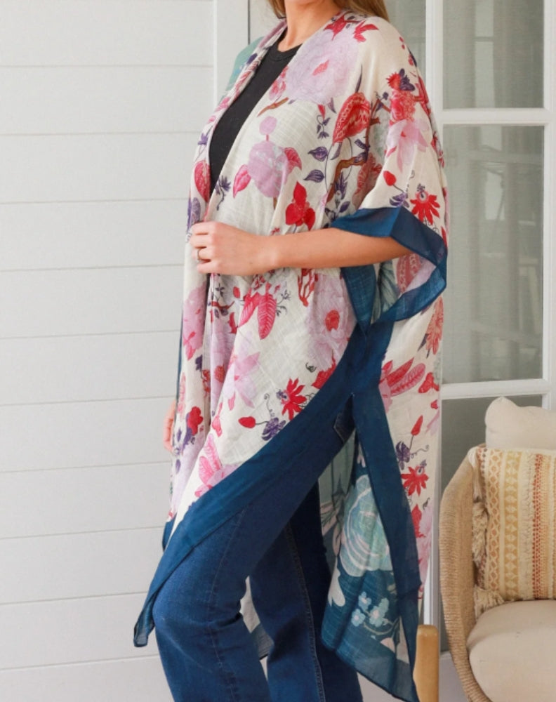 size 10 woman wearing a floral kimono over a black top and blue jeans, standing against a white wall.