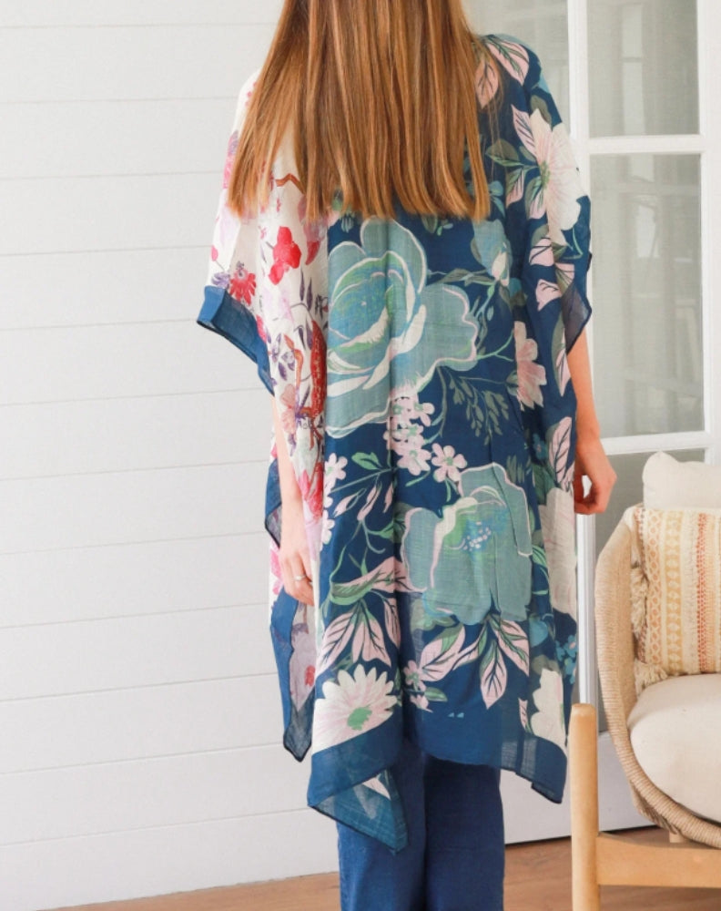 woman wearing a floral pink and navy kimono in a room with a white wall and chair.