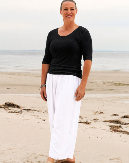 woman on beach wearing black scoop tee and 7/8 relaxed resort pants in white rayon with wide leg