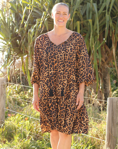 Woman wearing a beach boho style leopard print dress standing outdoors with greenery in the background