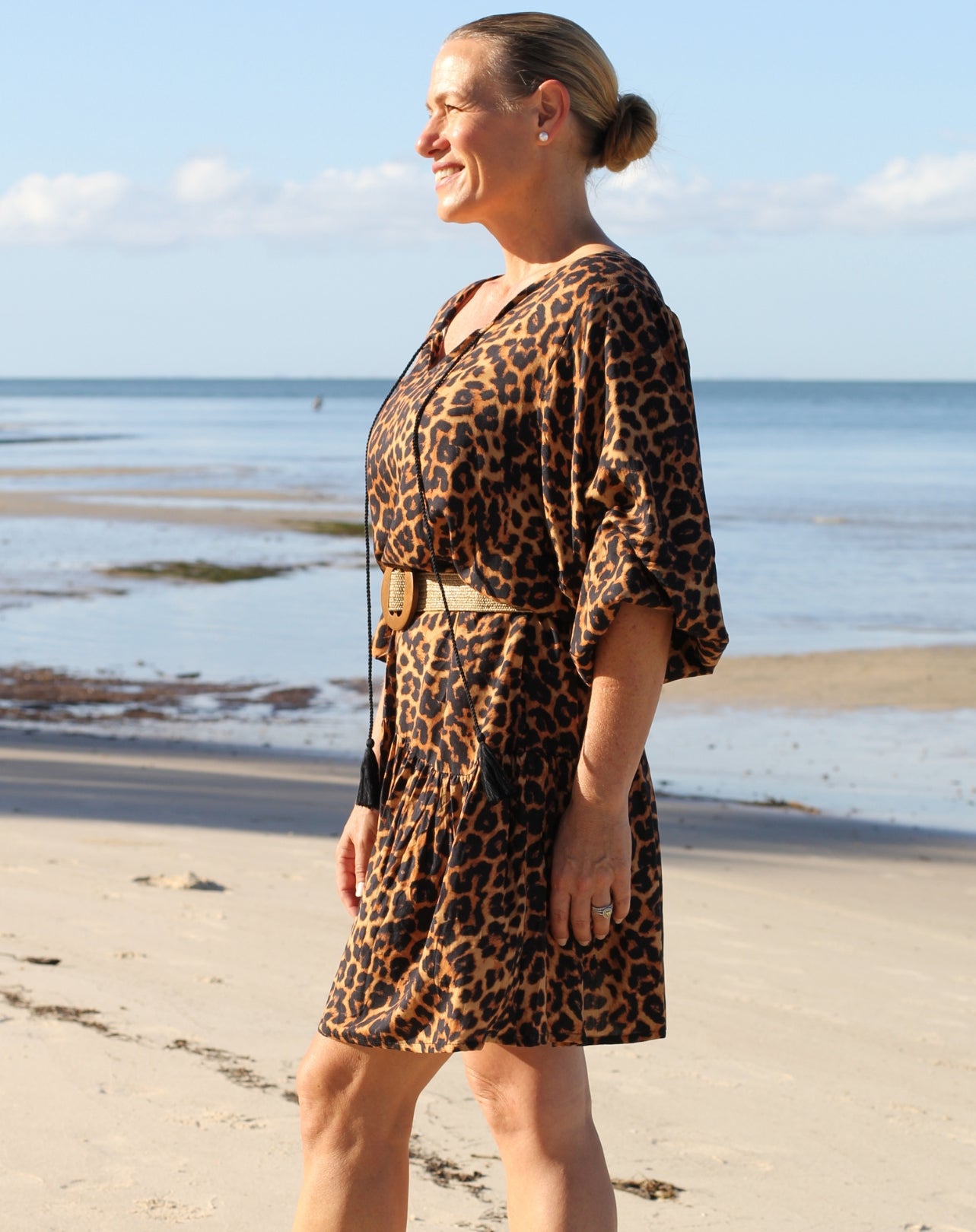 Woman wearing a leopard print boho dress standing on a beach.