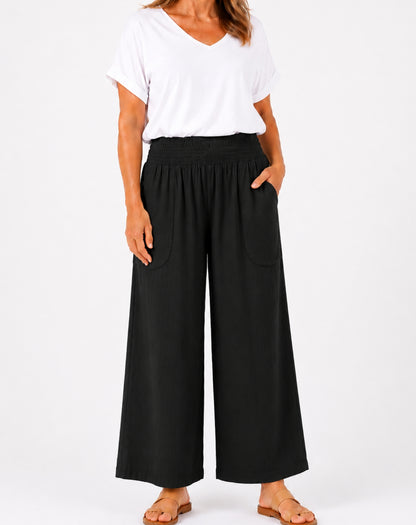A woman wearing black wide-leg cropped pants with side pockets, paired with a white V-neck t-shirt and flat sandals, shown against a plain white studio background.