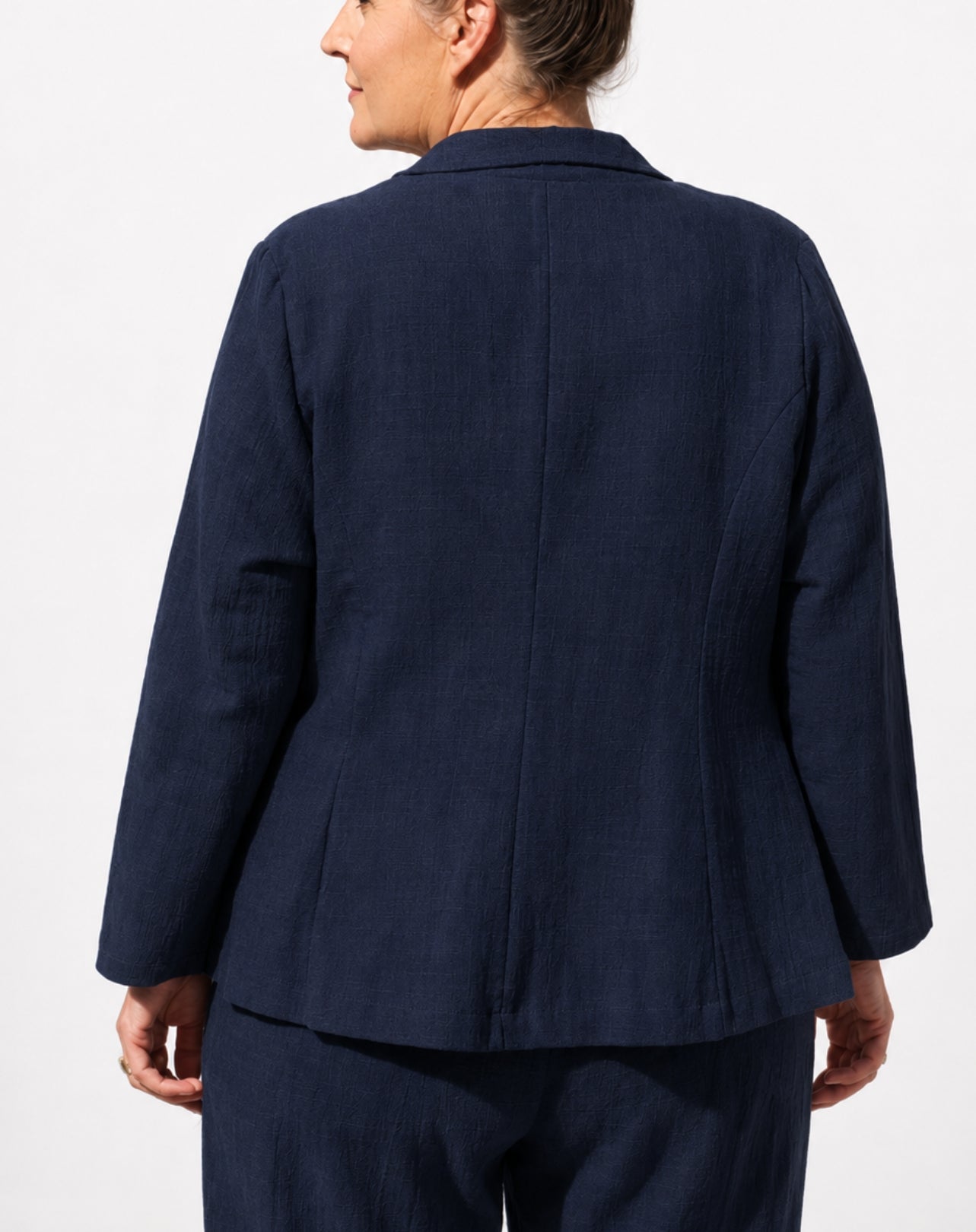 A woman shown from the back wearing a dark navy blue tailored cotton linen jacket and matching trousers against a plain light background.