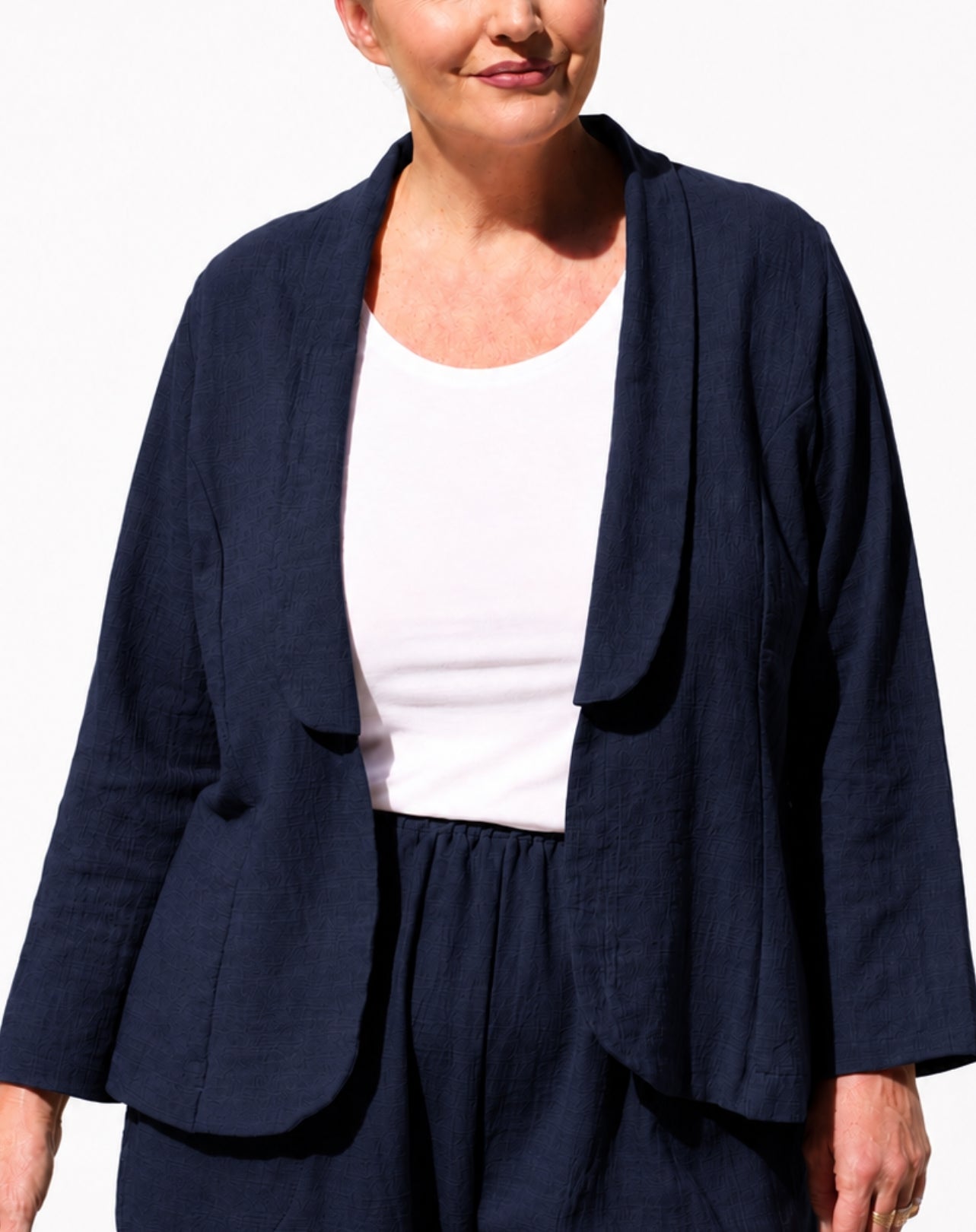 A woman wearing a navy blue open-front linen-blend jacket over a white tank top and matching navy trousers, photographed against a clean white background.