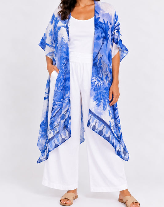 A woman modeling a lightweight blue and white tropical print kimono cardigan over a white tank top and white wide-leg pants, standing against a plain white studio background.