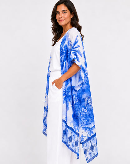 A woman modeling a blue and white tropical print kimono cardigan over a white dress, photographed against a clean white studio background.