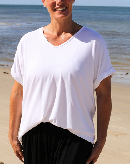Person wearing a white shirt modal tee and black pants standing on a beach.