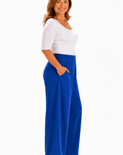 A woman wearing a white short-sleeve scoop-neck top and bright cobolt blue wide-leg pants with side pockets, shown against a plain white background.