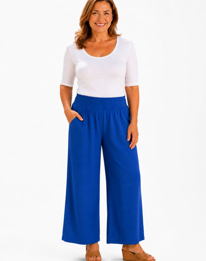A woman modeling a white short-sleeve scoop-neck top and bright cobolt blue wide-leg pants against a plain white studio background.