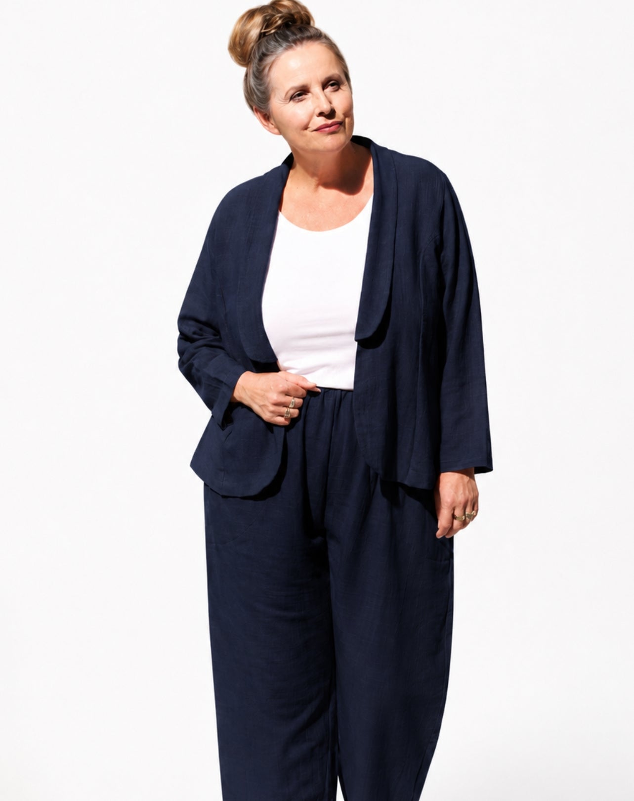 A woman modeling a navy blue two-piece pantsuit consisting of a draped open-front blazer and matching wide-leg trousers, worn over a white top, against a plain white background.