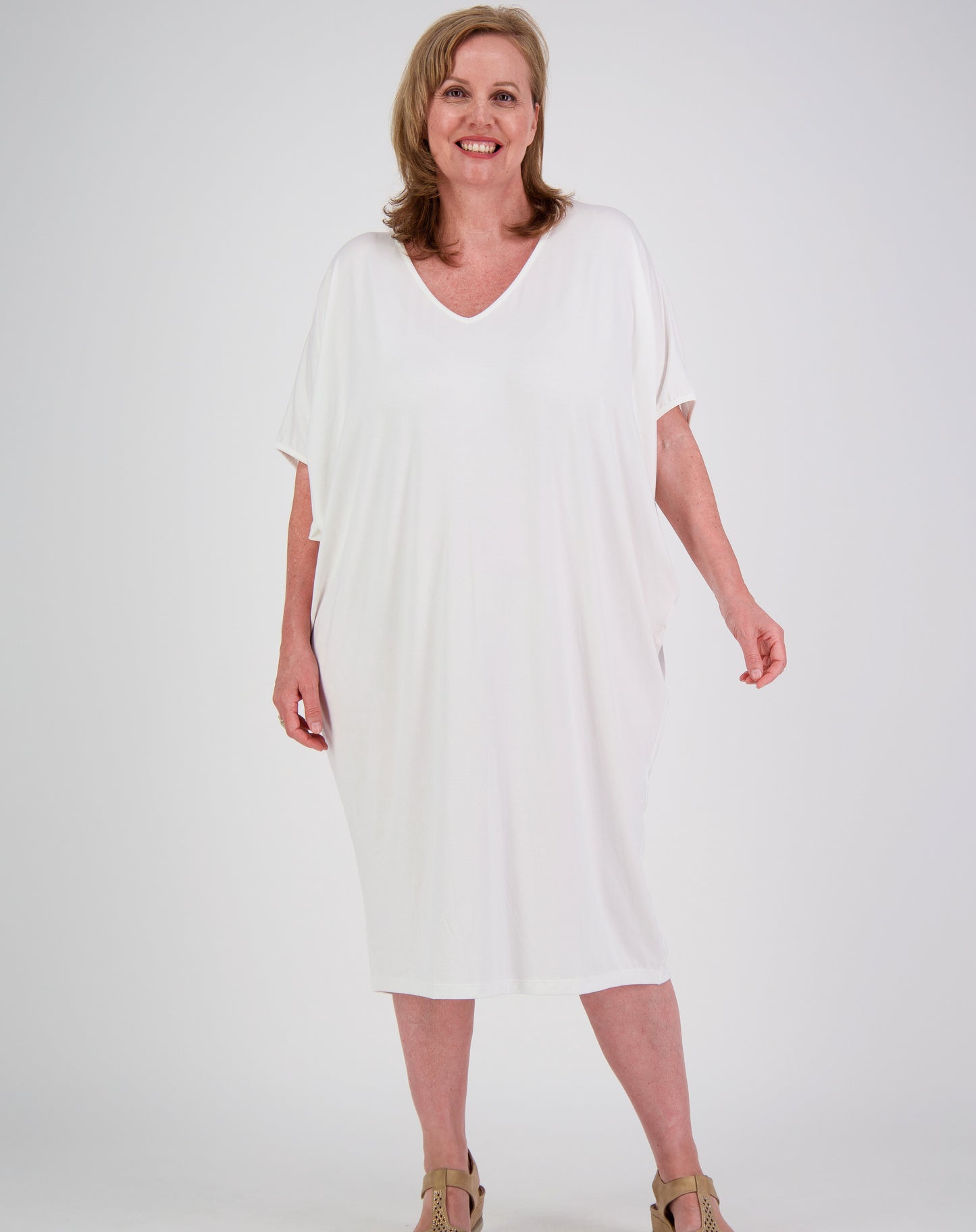 Woman wearing a white modal dress with batwing style on a plain background