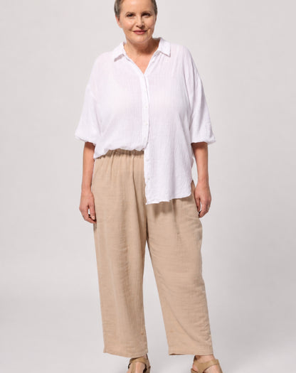 A woman modelling a white comfort cotton shirt adjustable sleeves button-up shirt and beige wide-leg pants against a light grey studio background.