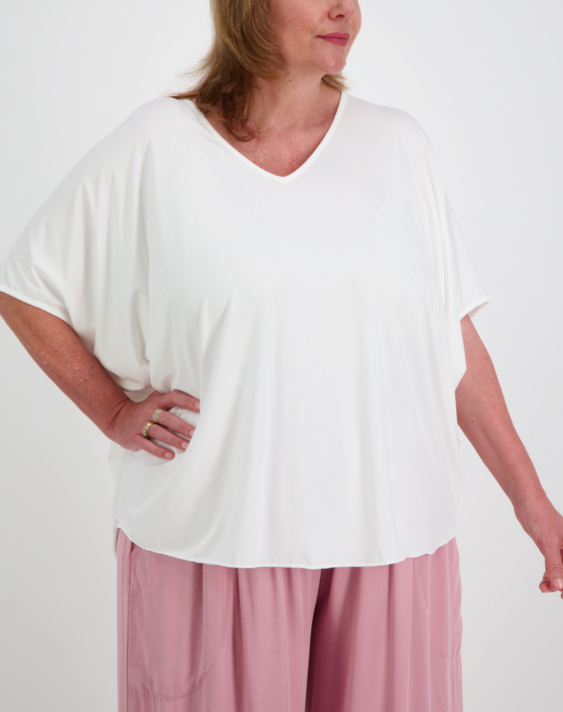 size 16 model wearing a white modal top in a batwing style and pink pants on a plain background