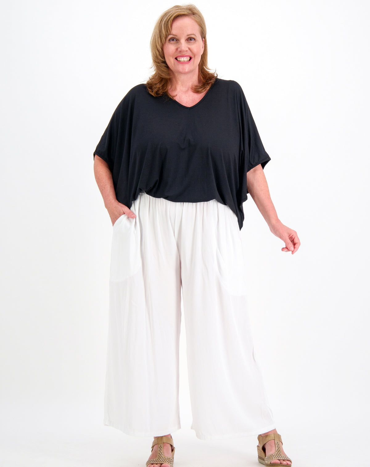A woman modeling a black short-sleeve V-neck top and white wide-leg pants against a plain white studio background.