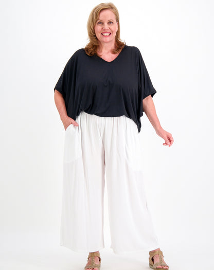 A woman modeling a black short-sleeve V-neck top and white wide-leg pants against a plain white studio background.