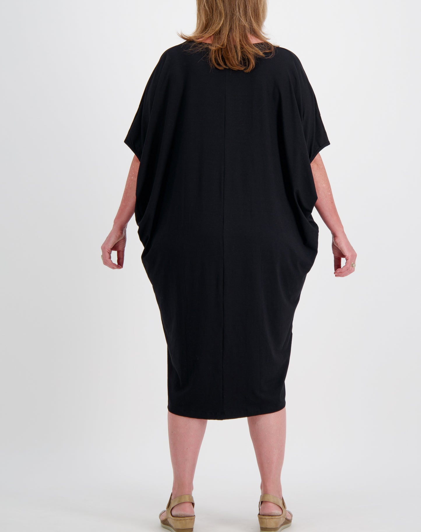 black comfort dress in black modal showing batwing style drape worn by a mature woman on a white background