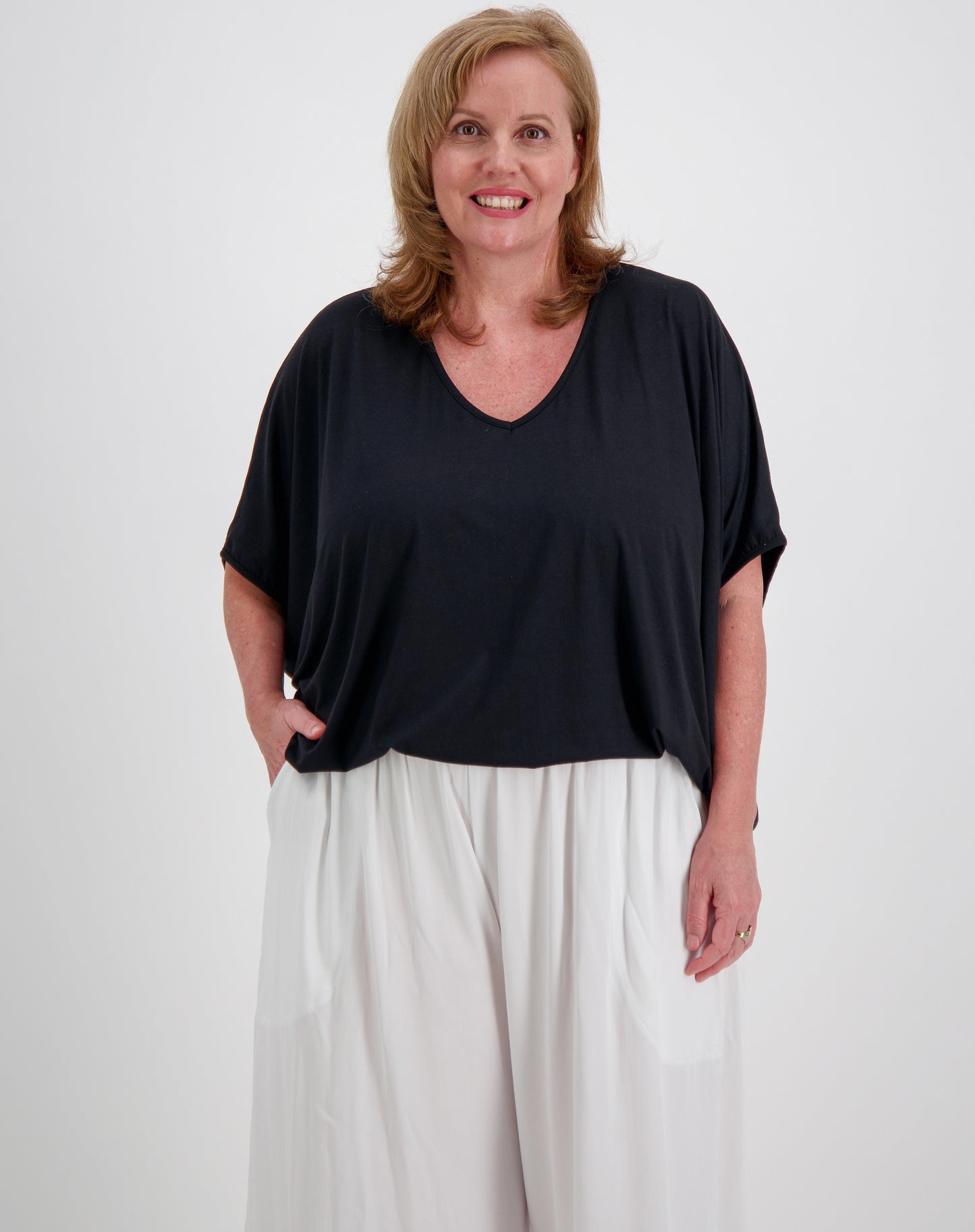 Woman wearing a black modal drape top and white everyday pants against a white background
