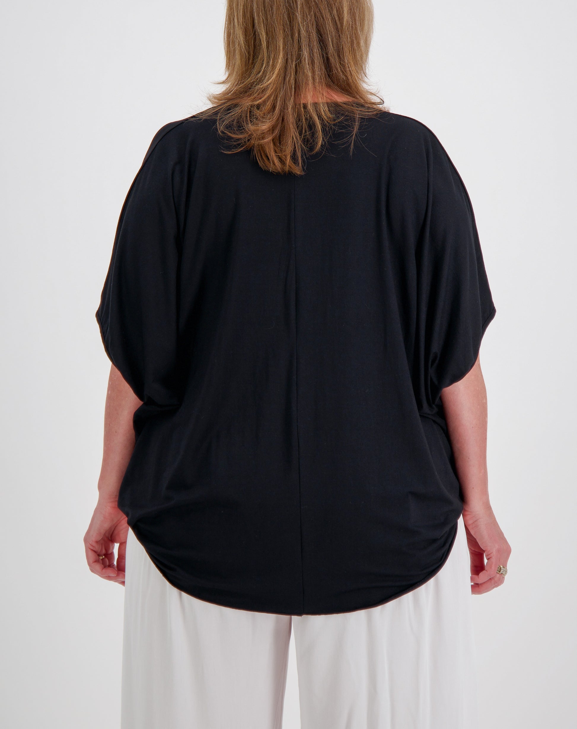 Person wearing a black modal top  with curved hem and white pants on a white background