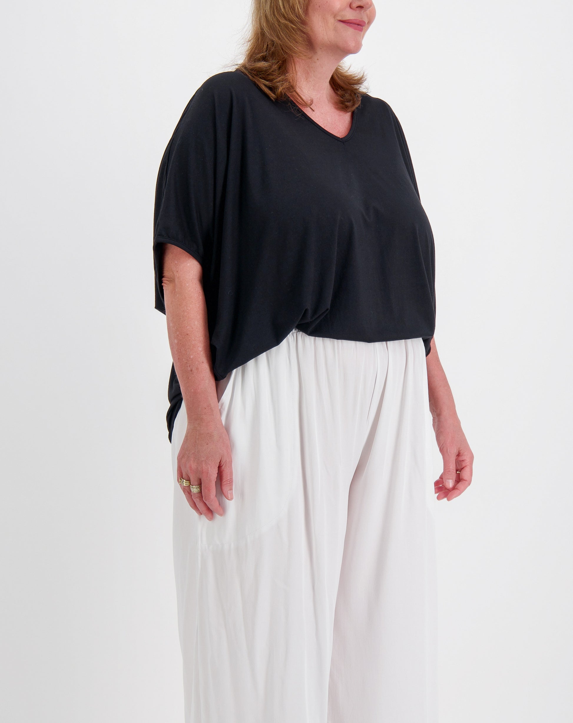 side view of woman wearing a black comfort top and white pants on a plain background