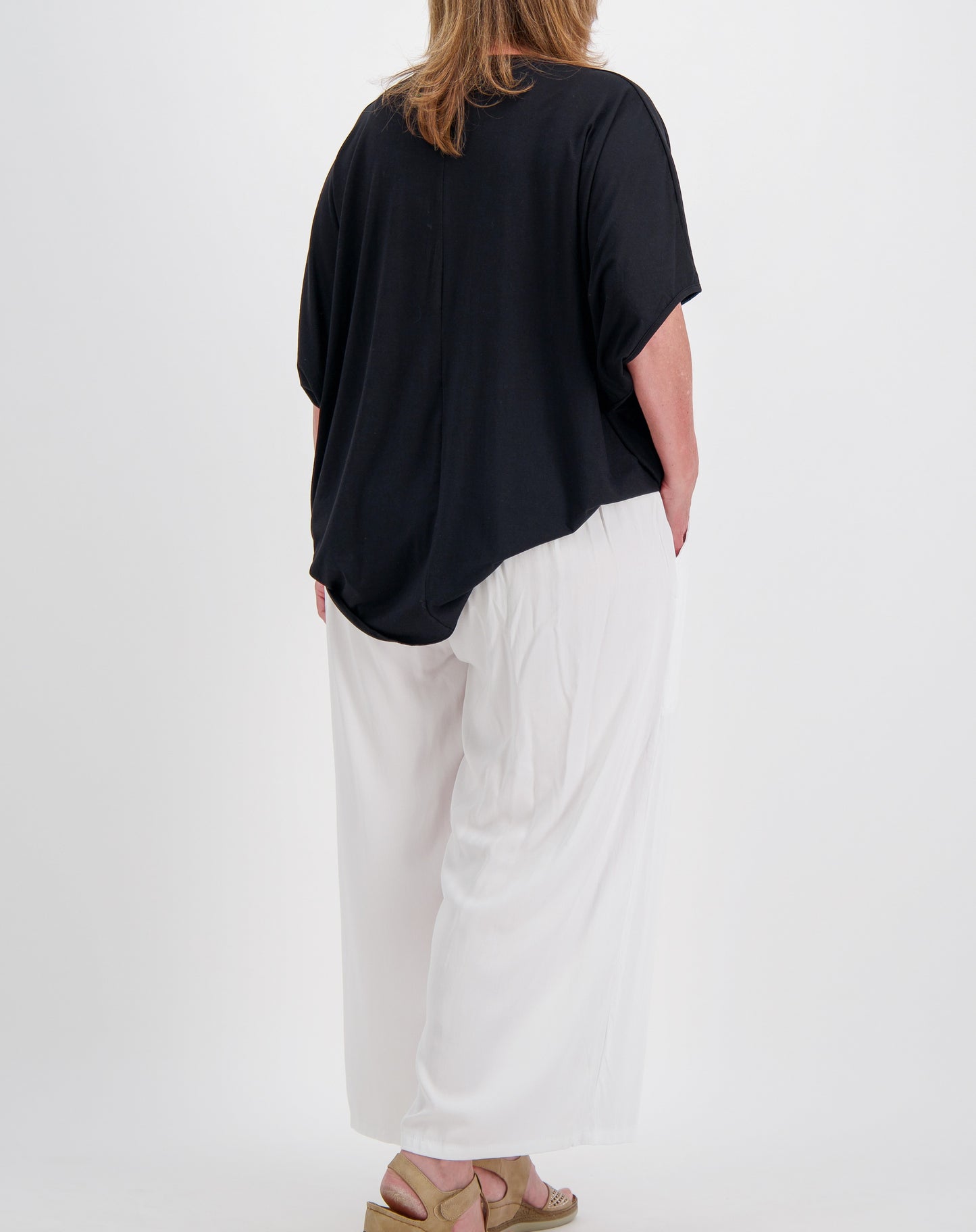 size 16 woman wearing a black comfort modal top with curved hem and white pants on a white background