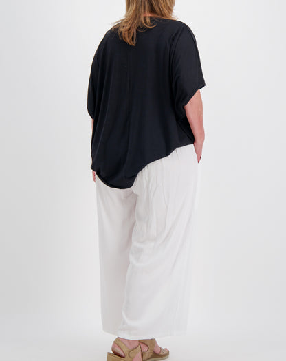 size 16 woman wearing a black comfort modal top with curved hem and white pants on a white background