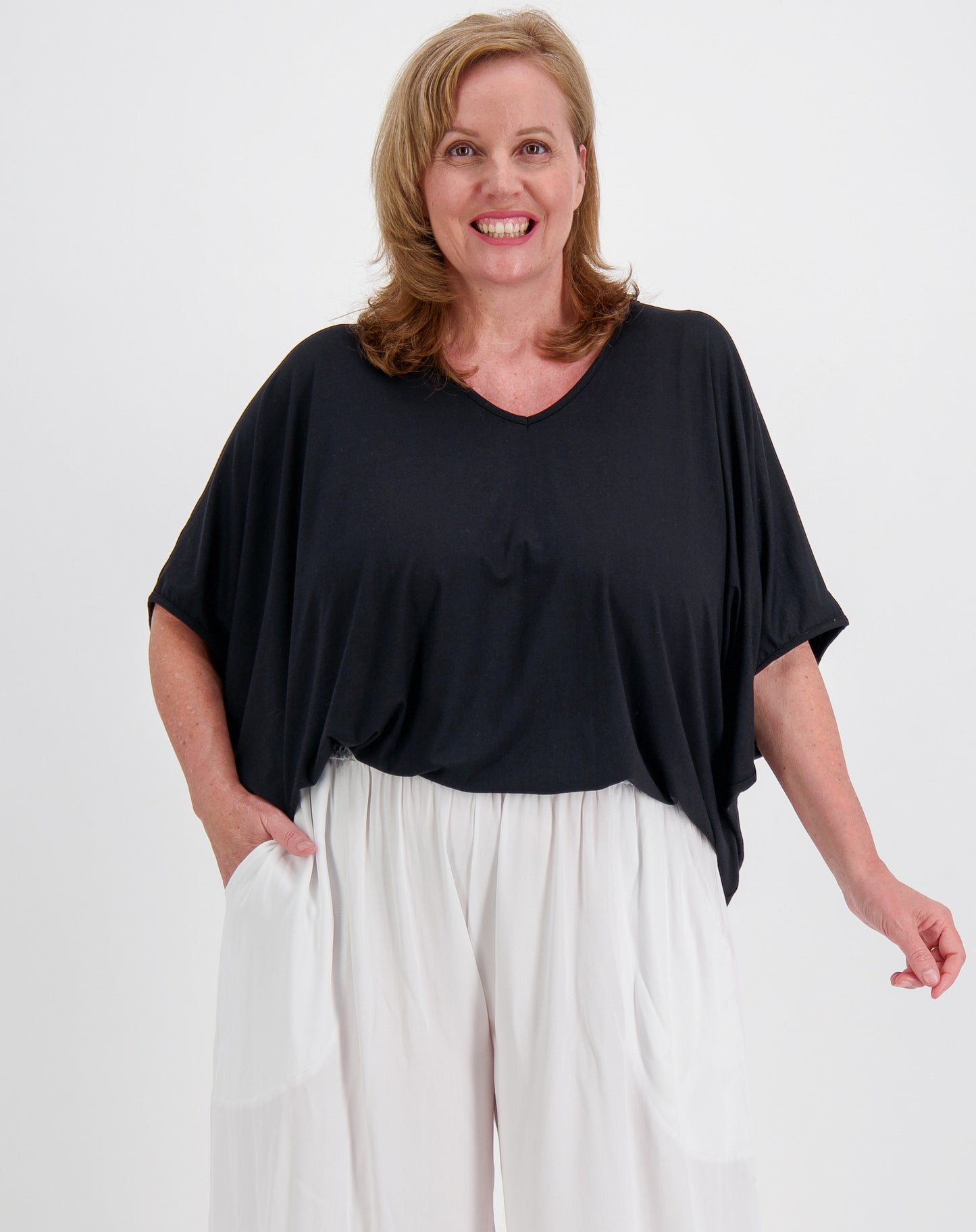 Woman wearing a black modal top and white resort  pants on a white background