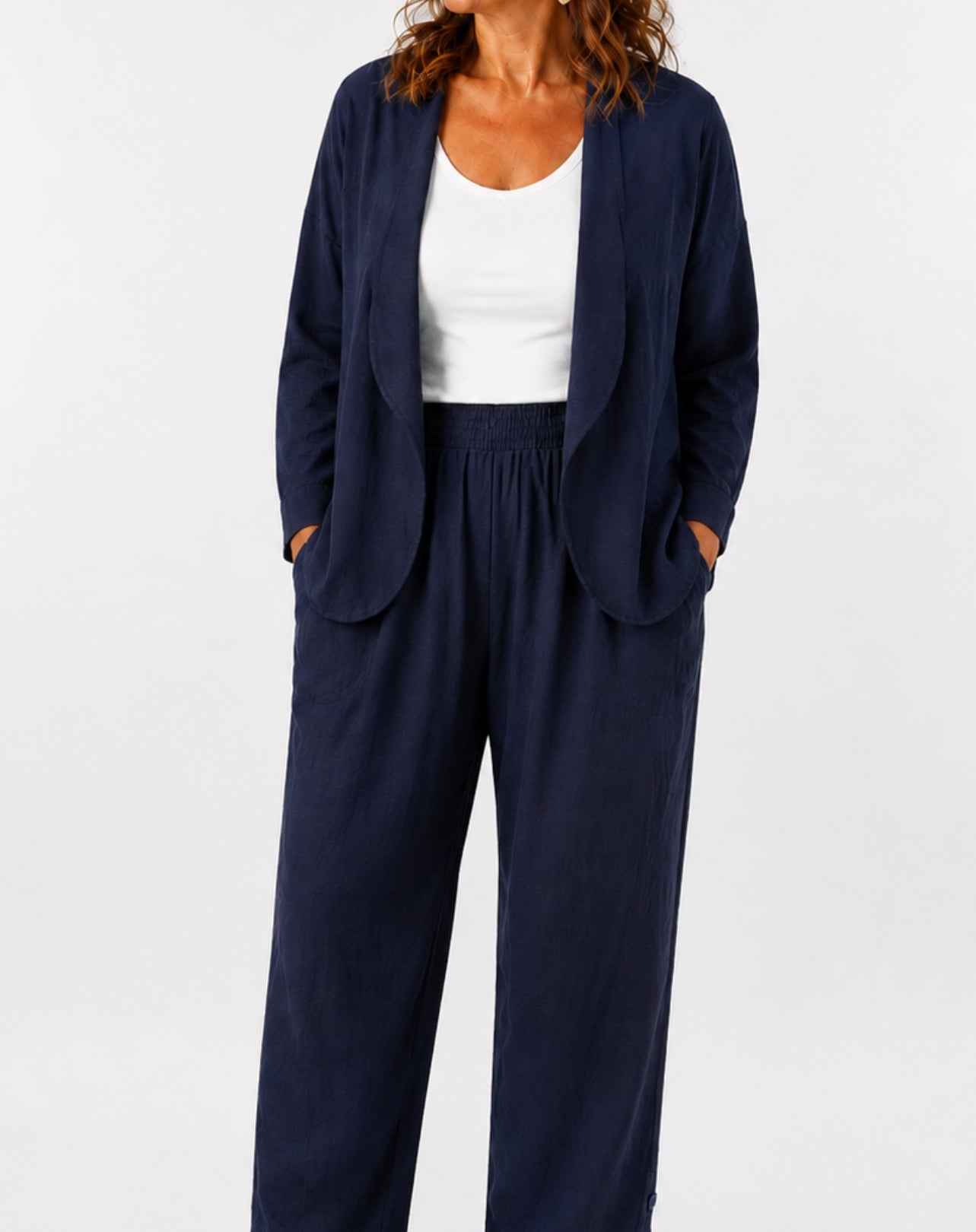 A woman wearing a navy blue open-front blazer and matching comfort wide-leg pants over a white tank top, shown against a plain light grey studio background.