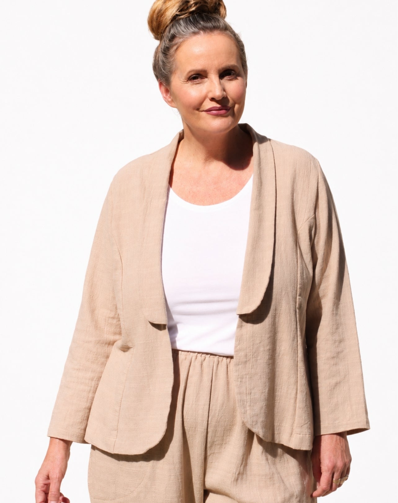 A woman wearing a light beige natural linen-blend jacket and matching trousers over a white scoop top, photographed against a plain white background.