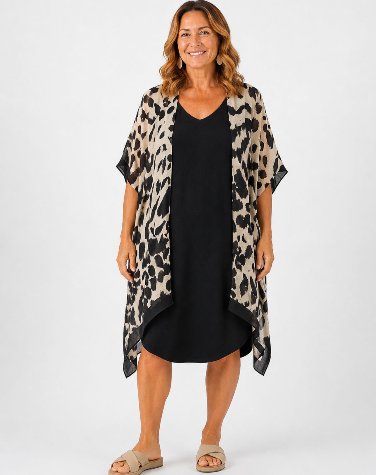 A woman modelling a leopard-print open-front kimono jacket over a black V-neck dress, standing against a plain light grey studio background.
