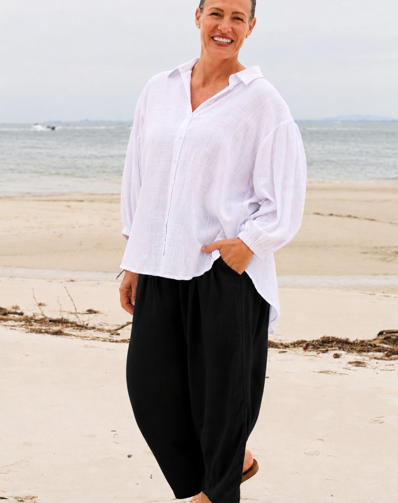 woman wearing black wide leg pant and white beach shirt standing on the sand at Bribie island