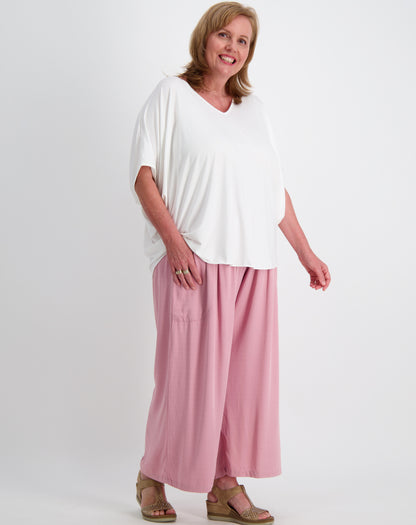 Woman wearing a white comfort top and blushed pink pants on a white background