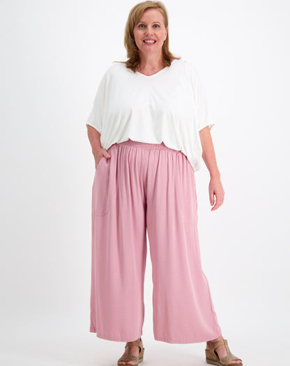 Woman wearing a white modal top and everyday blush pink pants on a white background