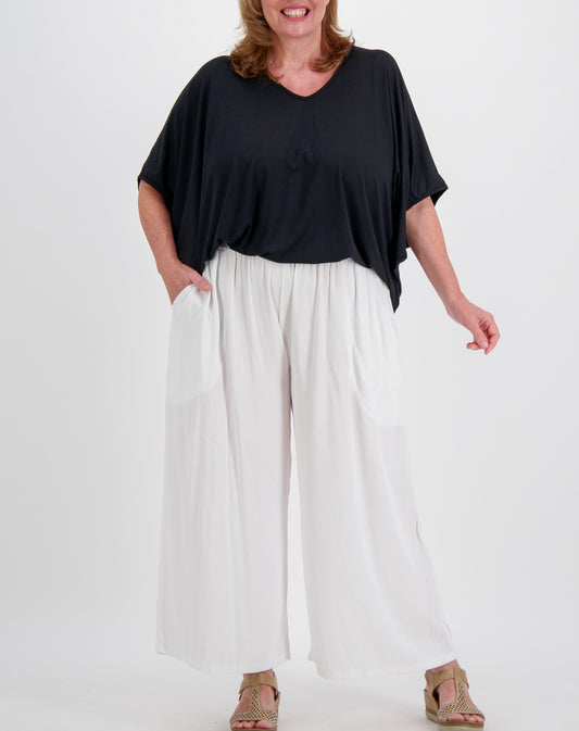 Woman wearing a black top and white wide leg every day pants on a white background