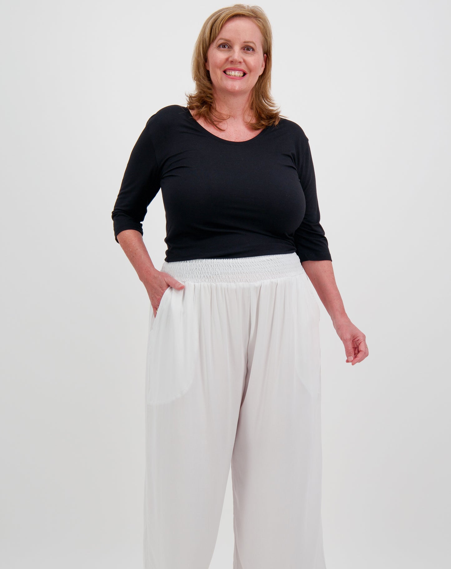 Woman wearing a black modal top and white resort pants on a plain background