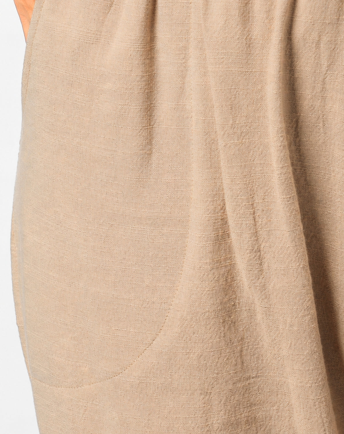 Close-up of a natural beige linen-textured garment with soft folds and a visible hand at the top left edge.