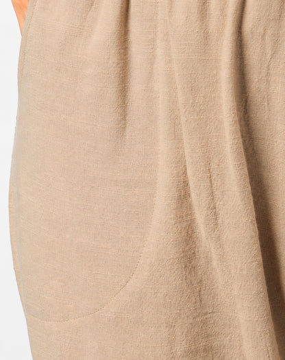 Close-up of a natural beige linen-textured garment with soft folds and a visible hand at the top left edge.