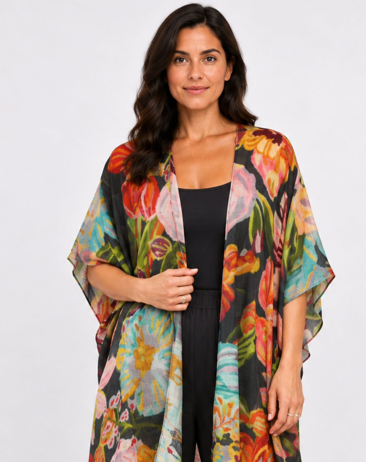 A woman modeling a lightweight open-front kimono cardigan with a vibrant multicolor floral print over a black jumpsuit, photographed against a solid light gray background.