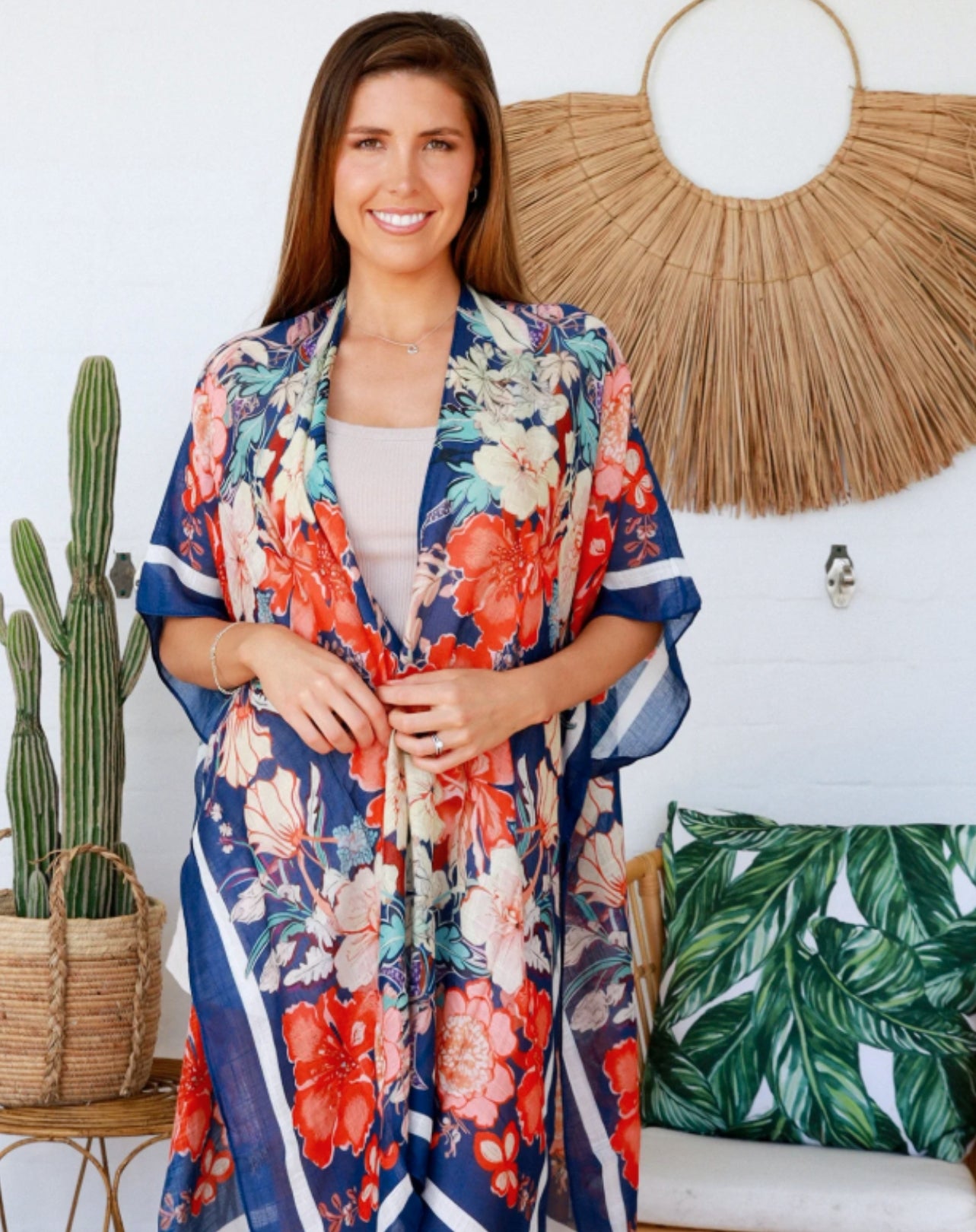 Woman wearing a blue hibiscus floral kimono in a room with decorative plants and wall art.