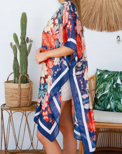 Person wearing a floral hibiscus kimono in a room with a cactus plant and leaf-patterned pillow.