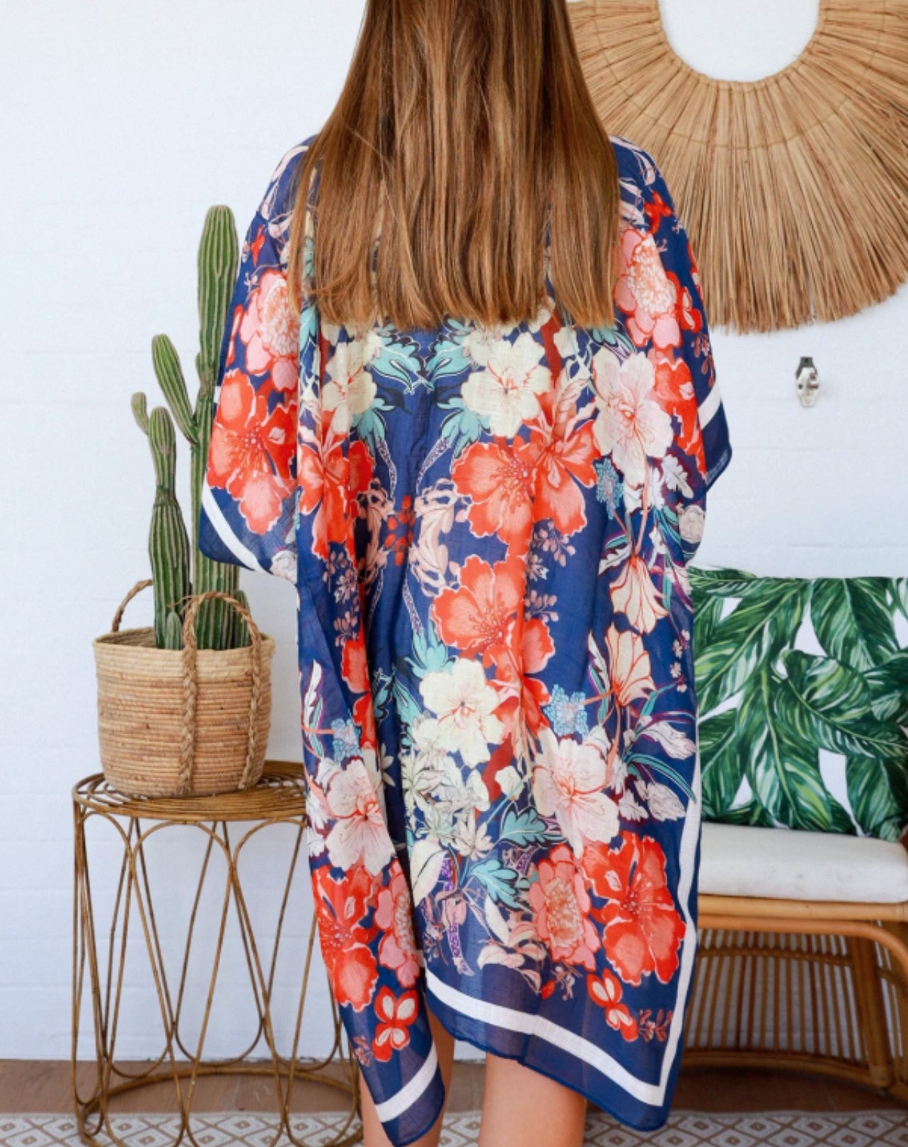 Person wearing a floral kimono in a boho inspired room with a plant and woven chair.