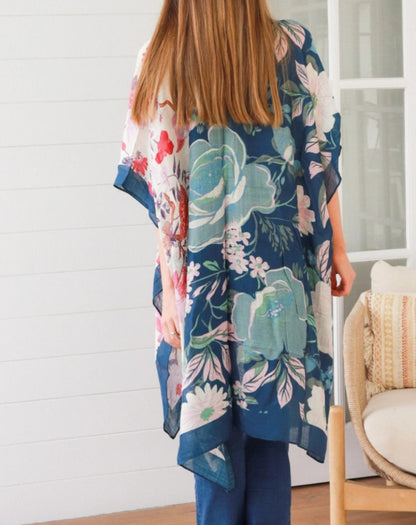 woman wearing  a floral pink and navy kimono in a room with a white wall and chair.