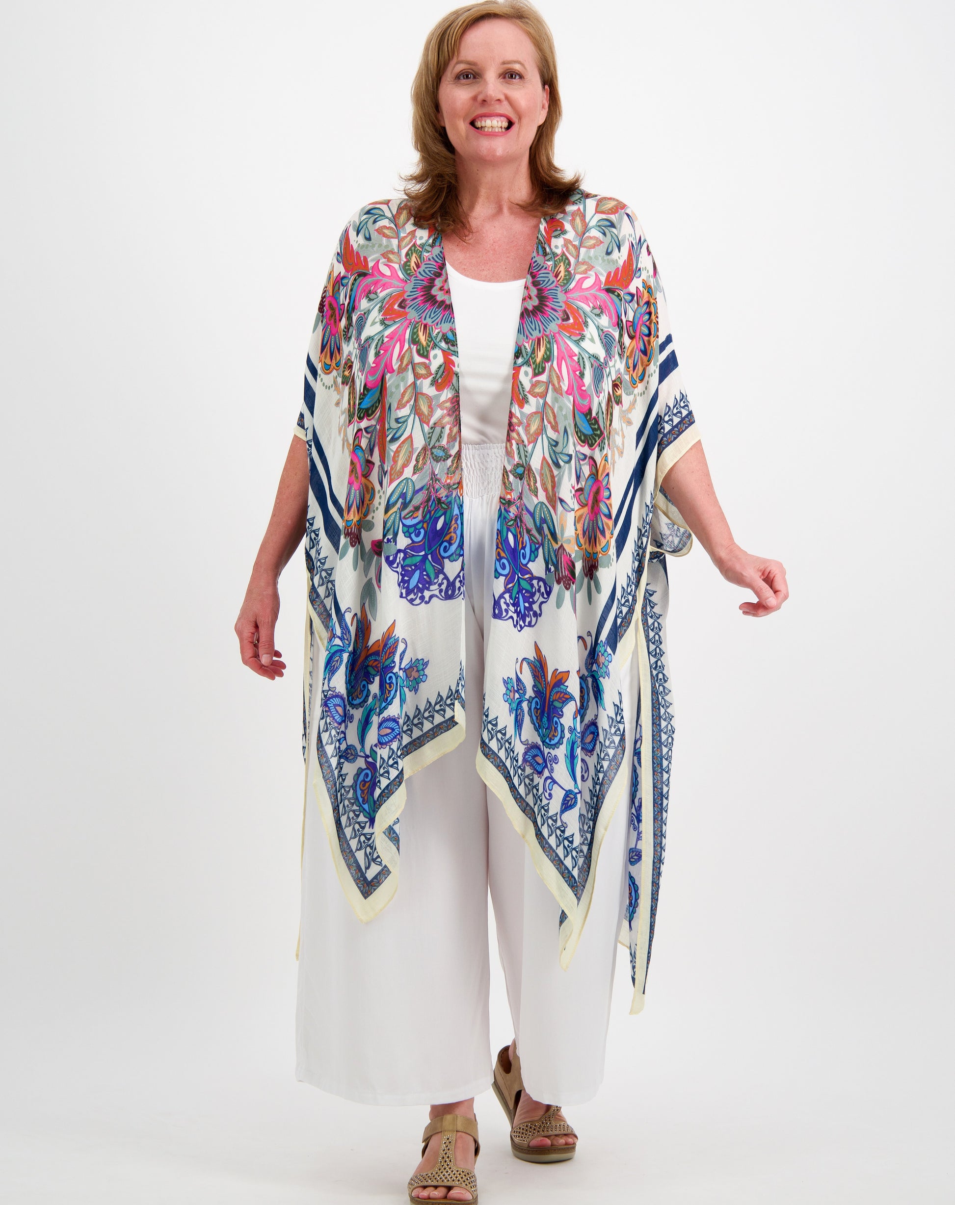 Woman in her 50s wearing a colorful boho floral kimono over a white  resort outfit  by miss seafari on a white background