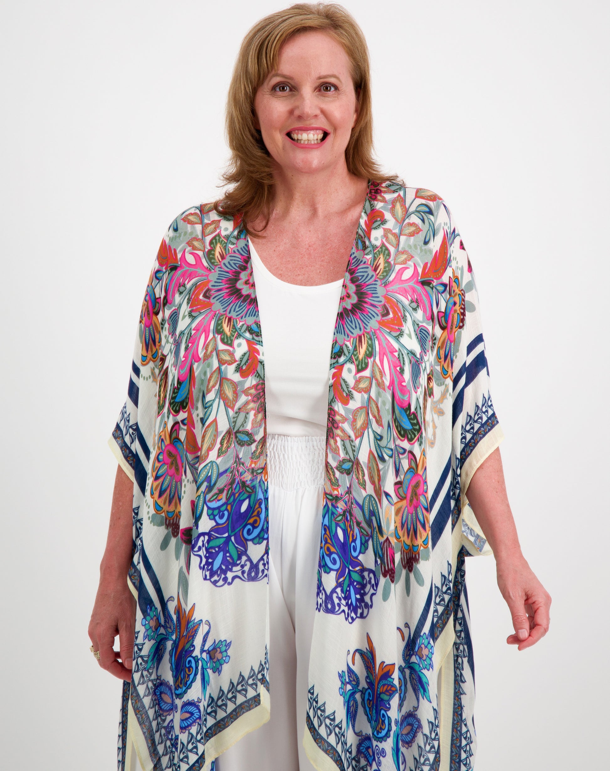 Woman wearing a boho kimono in pink and blue over a white outfit on a white background