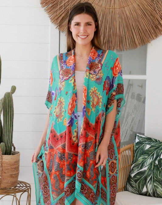 Woman wearing aqua camilla patterned kimono standing under a straw umbrella.