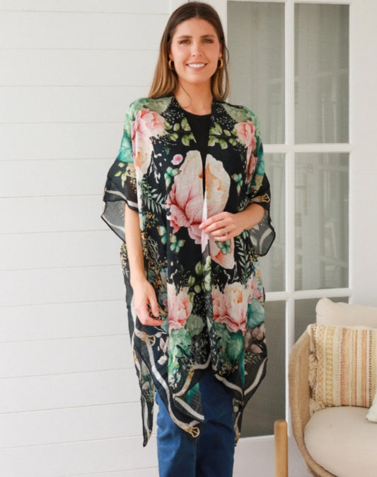 Woman wearing a floral kimono in a room with a white wall and a chair.