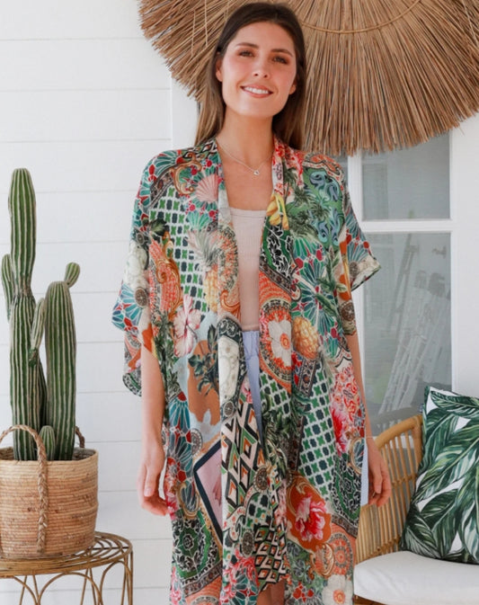 woman wearing kimono jacket in green morocan print in front of a boho decorated house