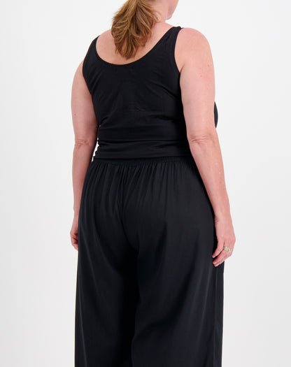 Person wearing a black sleeveless tank top in black and black pants on a white background