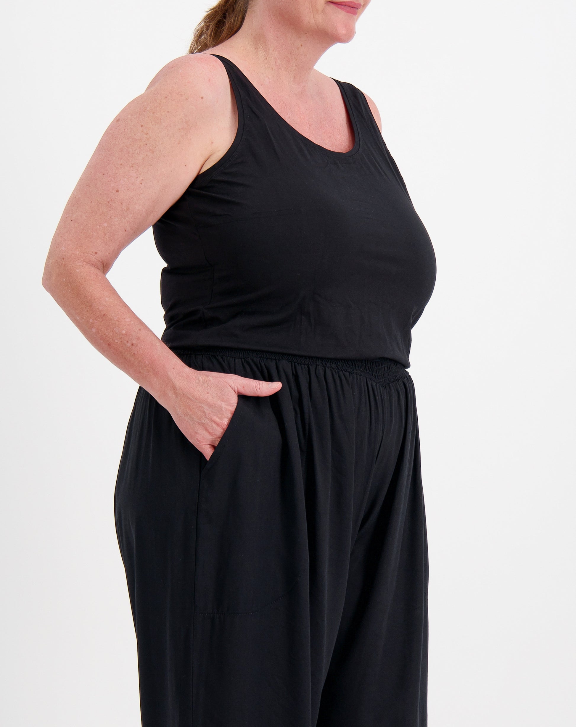 Person wearing a black sleeveless tank top in modal fabric and black pants on a white background